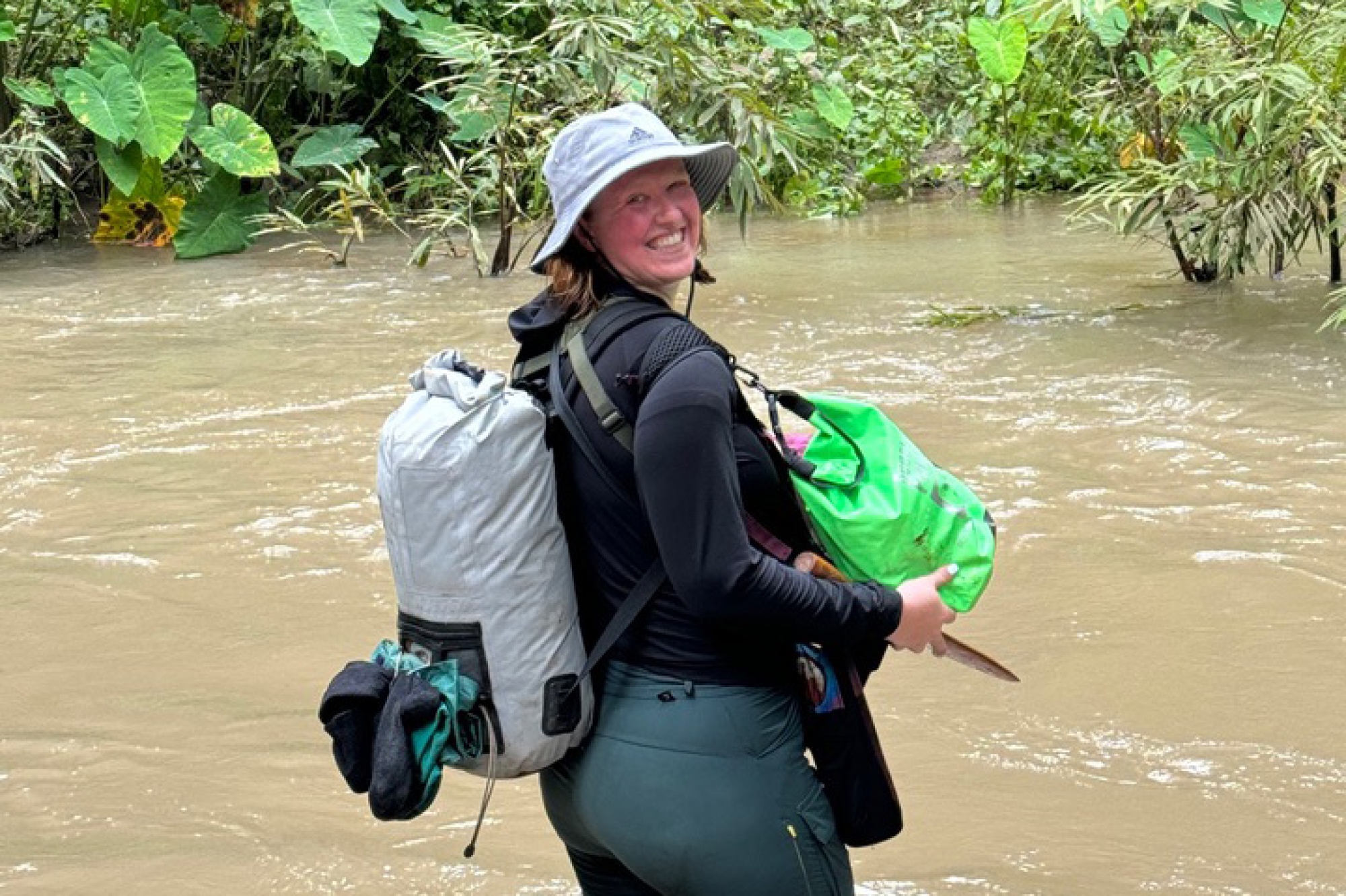 Person standing in water wearing a hat and two packs