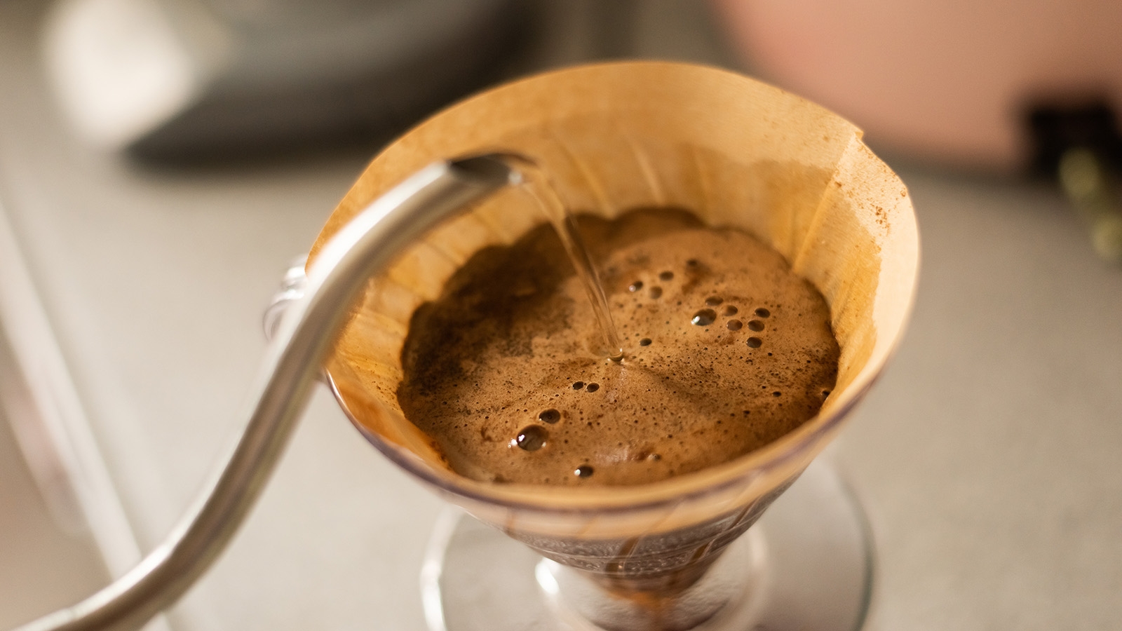 The spout of a long-necked kettle pouring water over a coffee filter. 