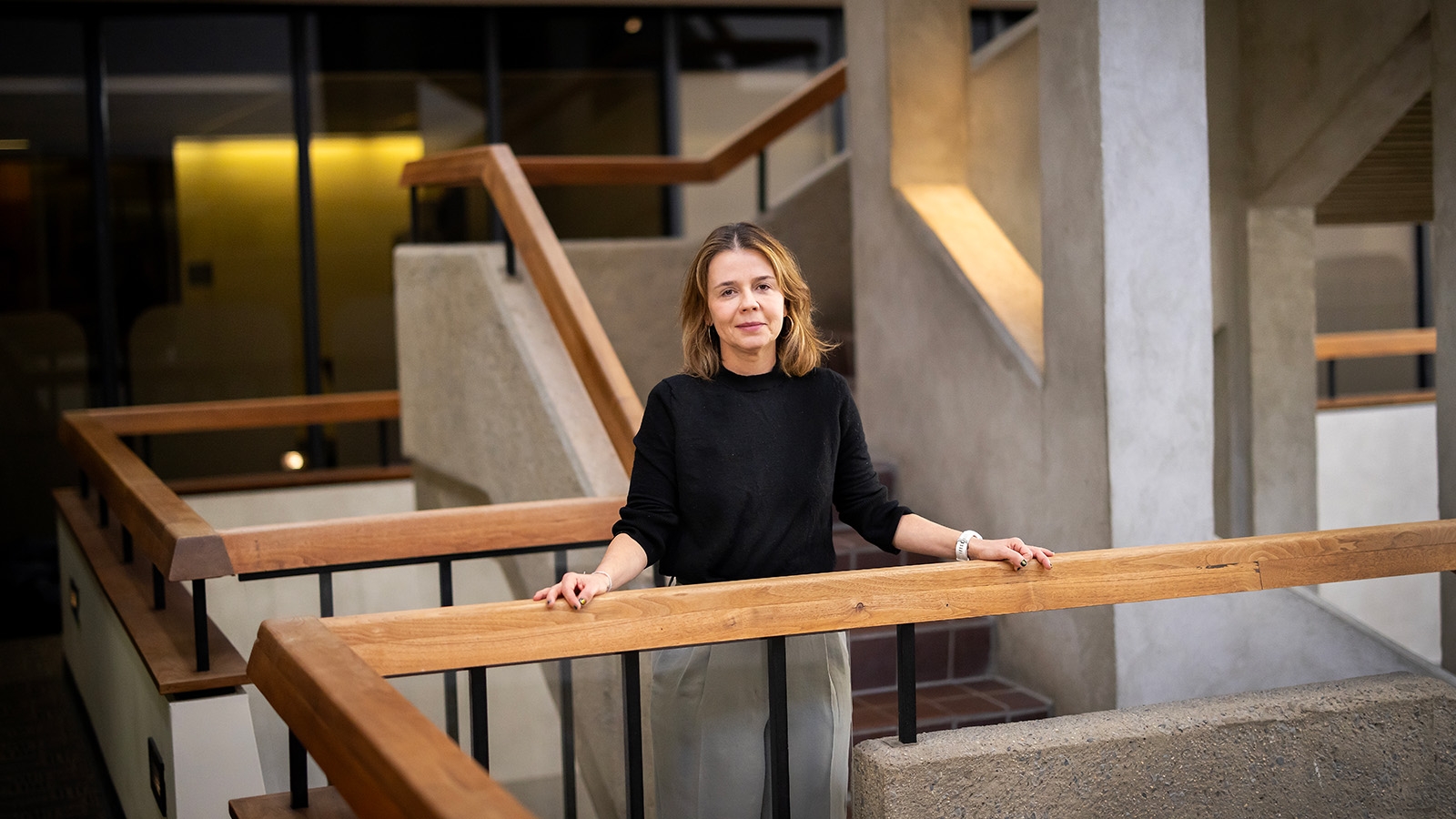 Leticia Marteleto standing at a balcony, with stairs and another balcony behind her.